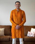 Man wearing an orange and yellow patterned kurta standing in a living room.