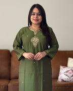 Woman wearing a green traditional outfit with embroidery in a living room setting.