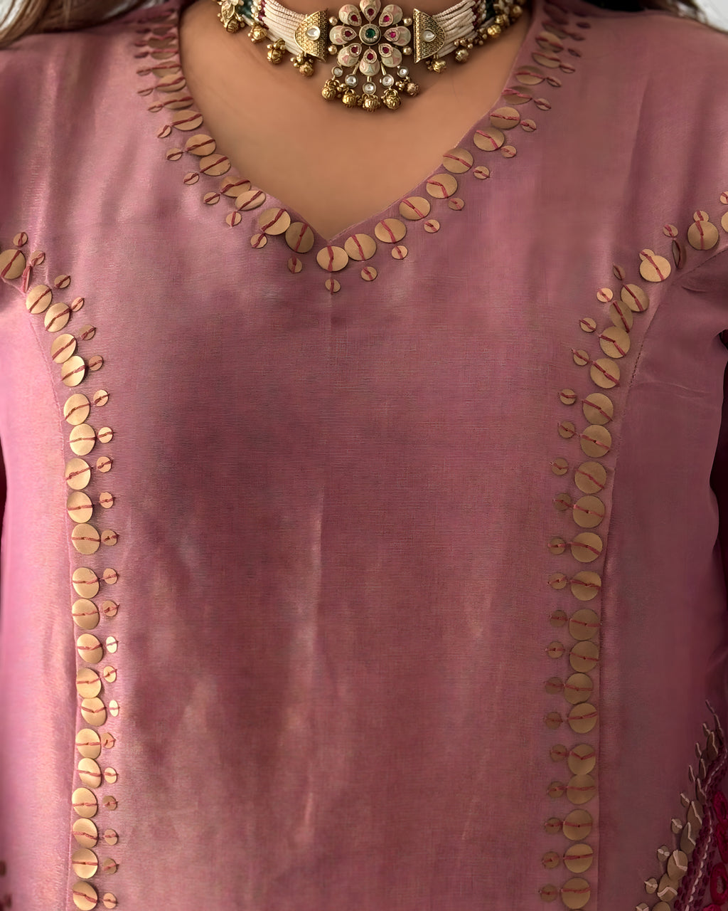 A close-up of a dusty pink traditional tunic with gold coin embroidery along the V-neckline and down the front panels, worn with a gold statement necklace.