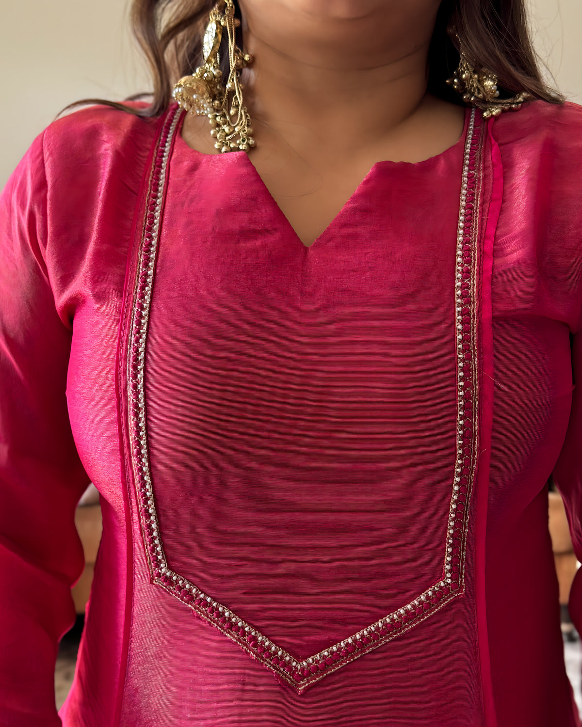 A close-up of a person wearing a bright pink traditional tunic top with gold embroidered trim along the neckline and a matching sheer pink dupatta draped over the shoulders.
