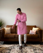 Man wearing a pink kurta with white pants standing in a living room.