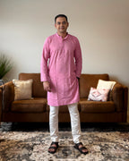Man wearing a pink kurta with white pants standing in a living room.