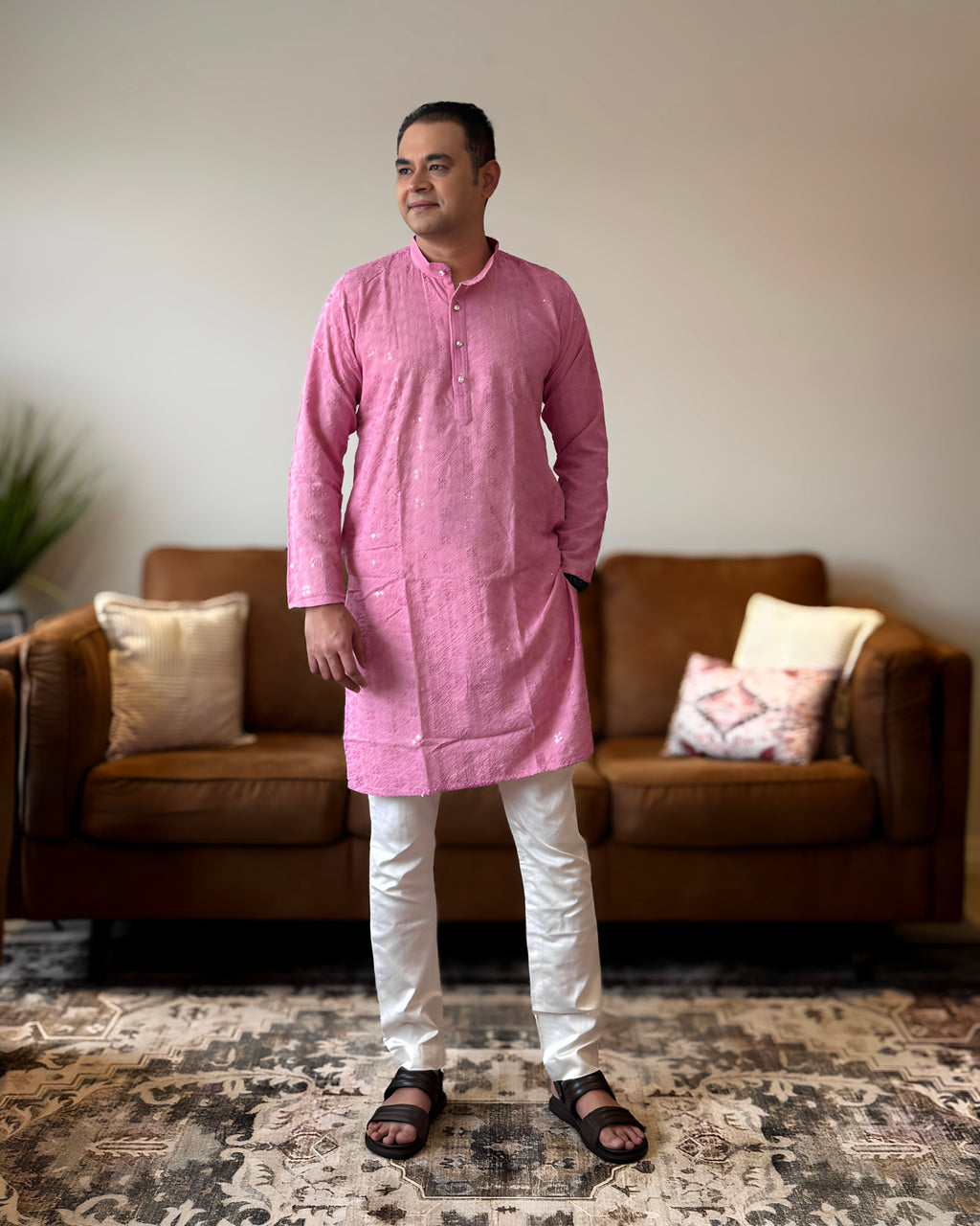 Man wearing a pink kurta with white pants standing in a living room.