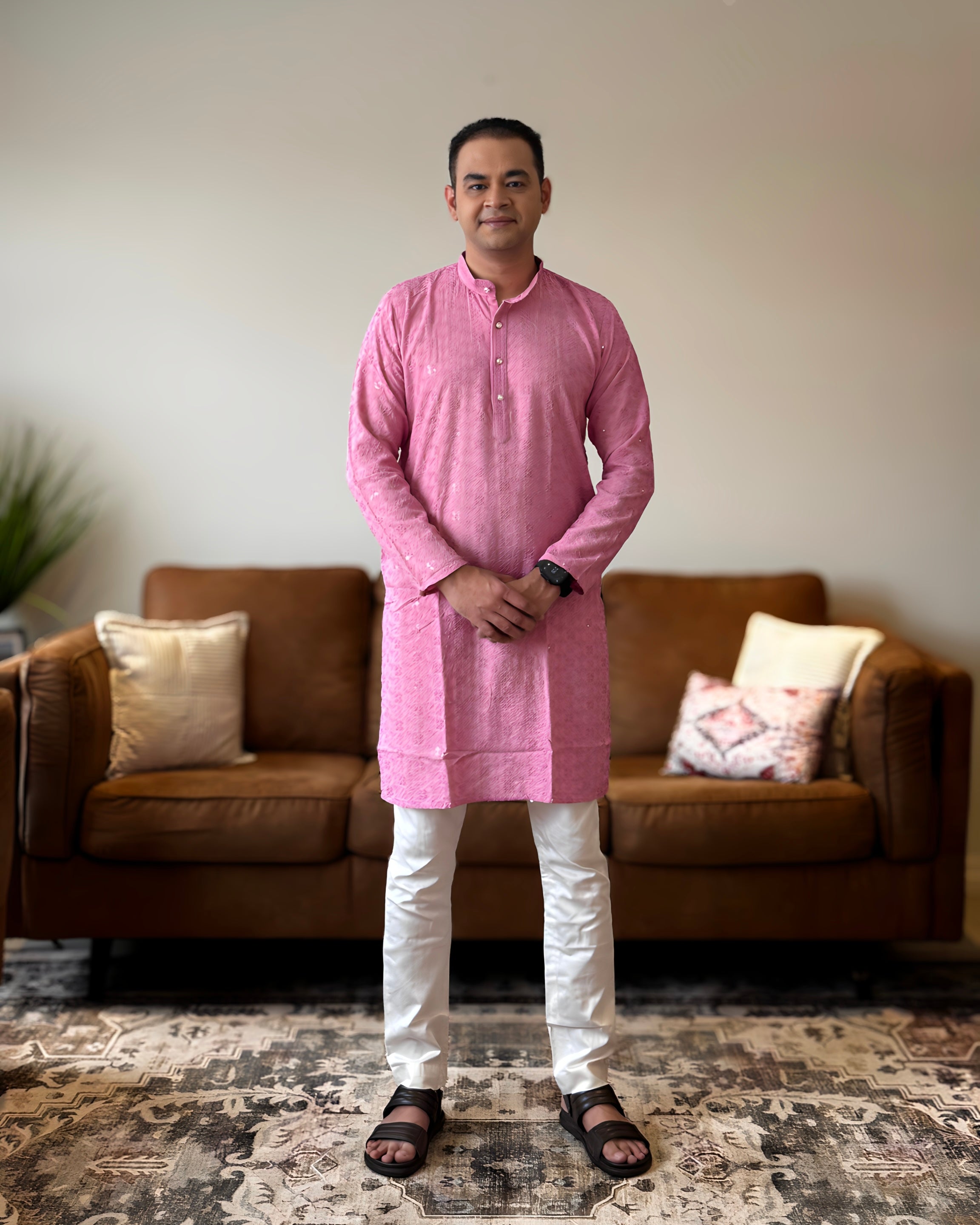 Man wearing a pink kurta with white pants standing in a living room.