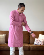 Man wearing a pink kurta standing in a living room with a brown sofa and patterned cushions.