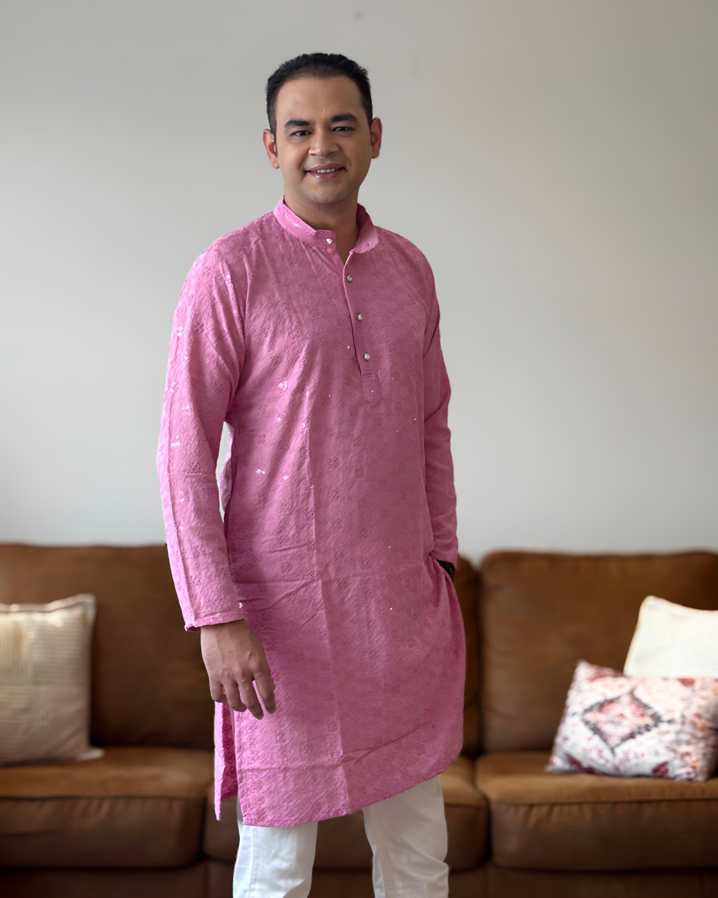 Man wearing a pink kurta standing in a living room with a brown sofa and decorative pillows.