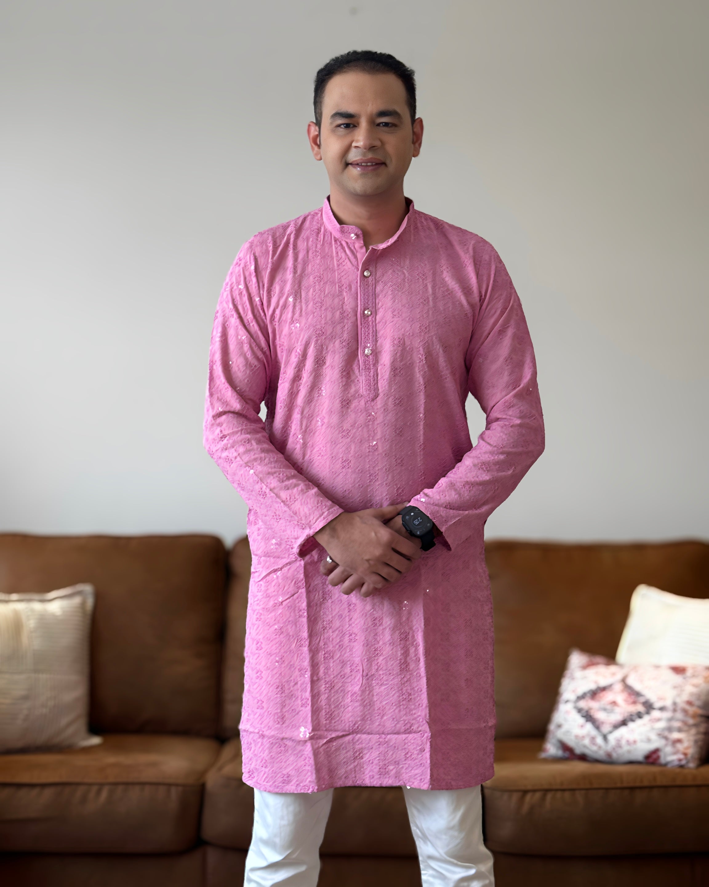 Man wearing a pink kurta standing in a living room with a brown sofa and decorative pillows.