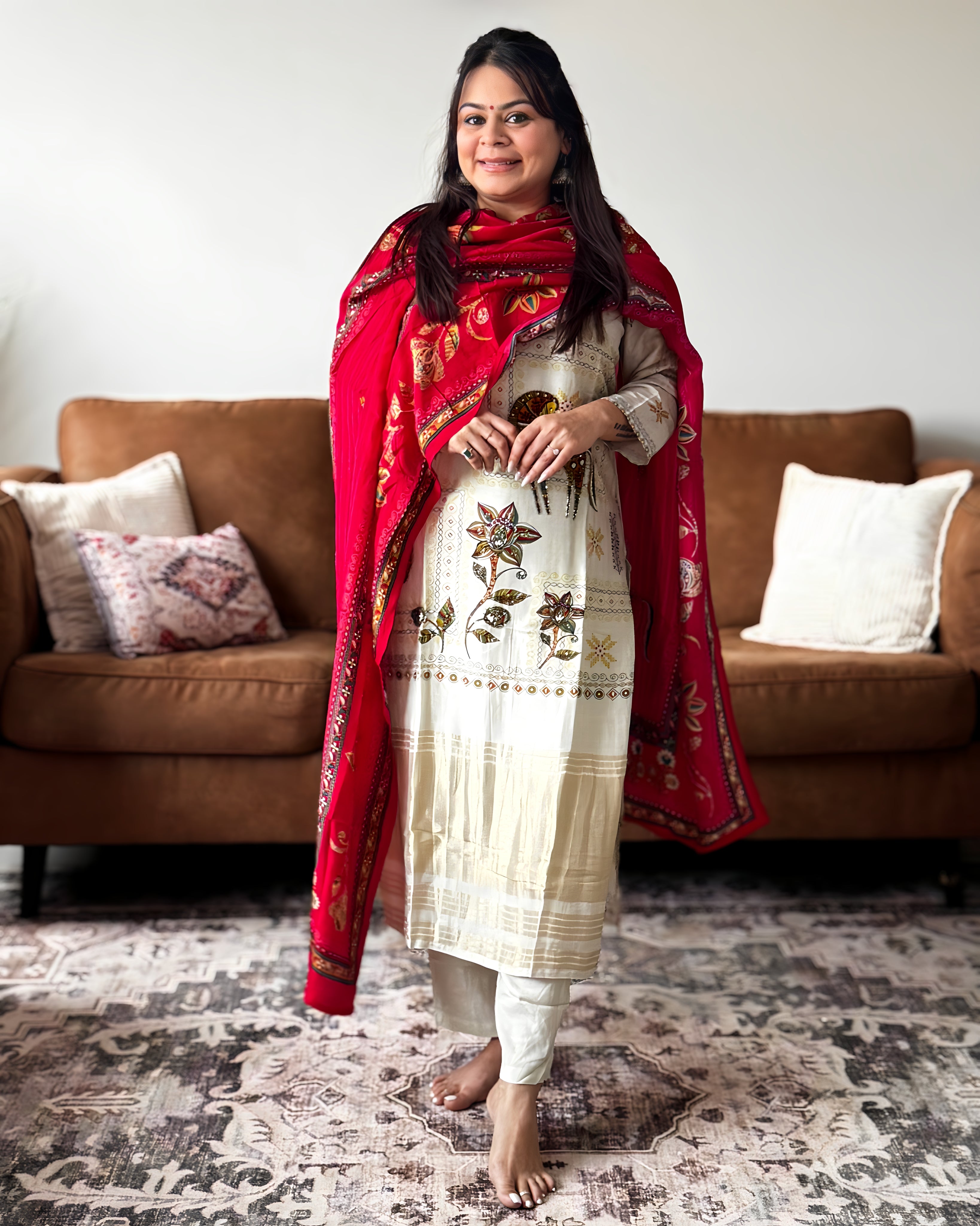 Woman in traditional outfit with red dupatta standing in a living room.