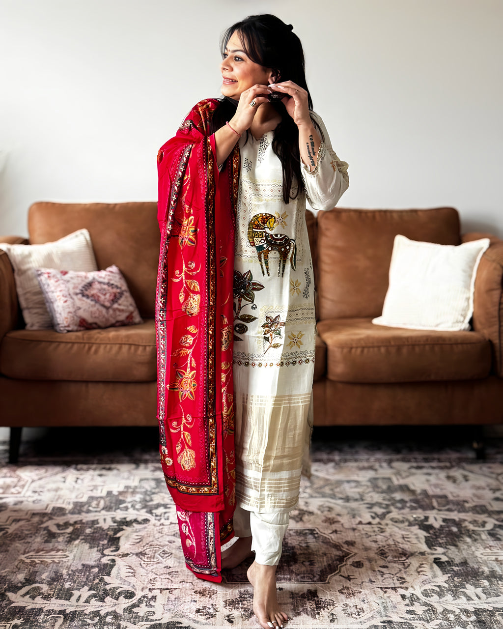 Woman in a white traditional outfit with a red scarf standing in a living room.