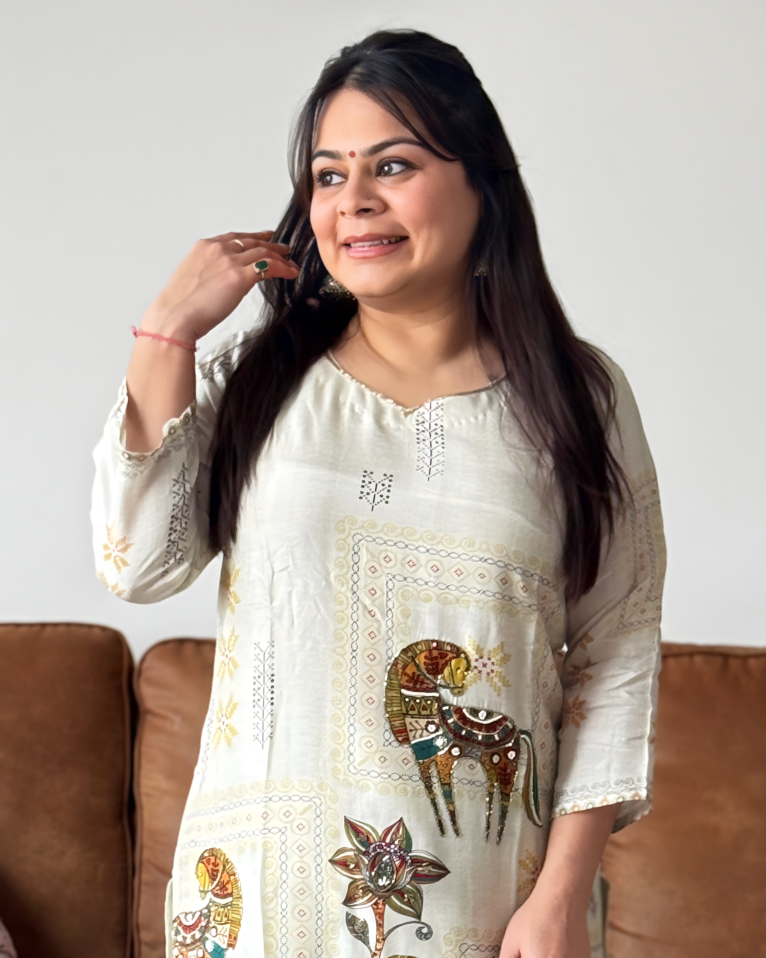 Woman wearing a white embroidered dress with a brown sofa in the background