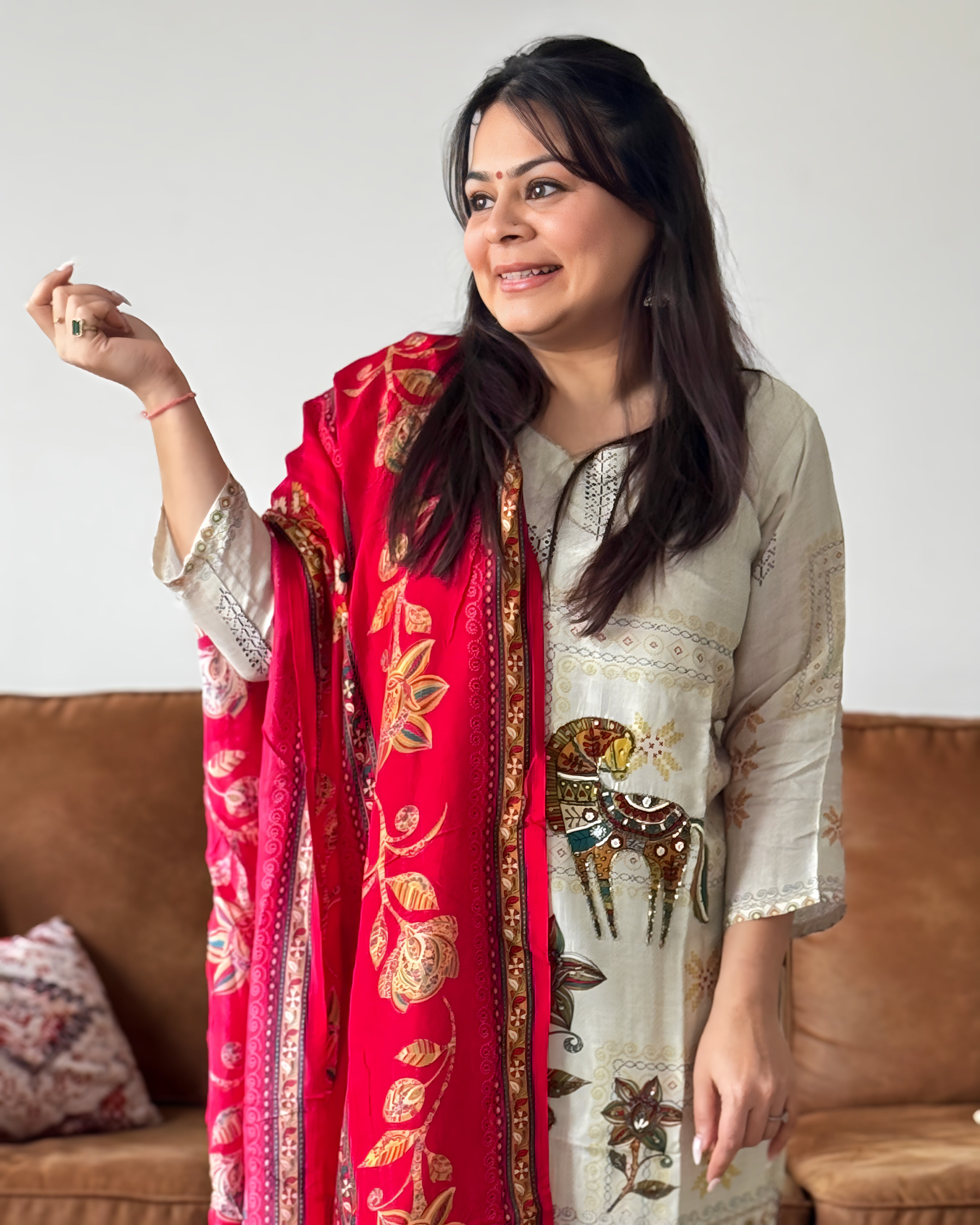 Woman holding a red and gold patterned scarf in front of a white wall.