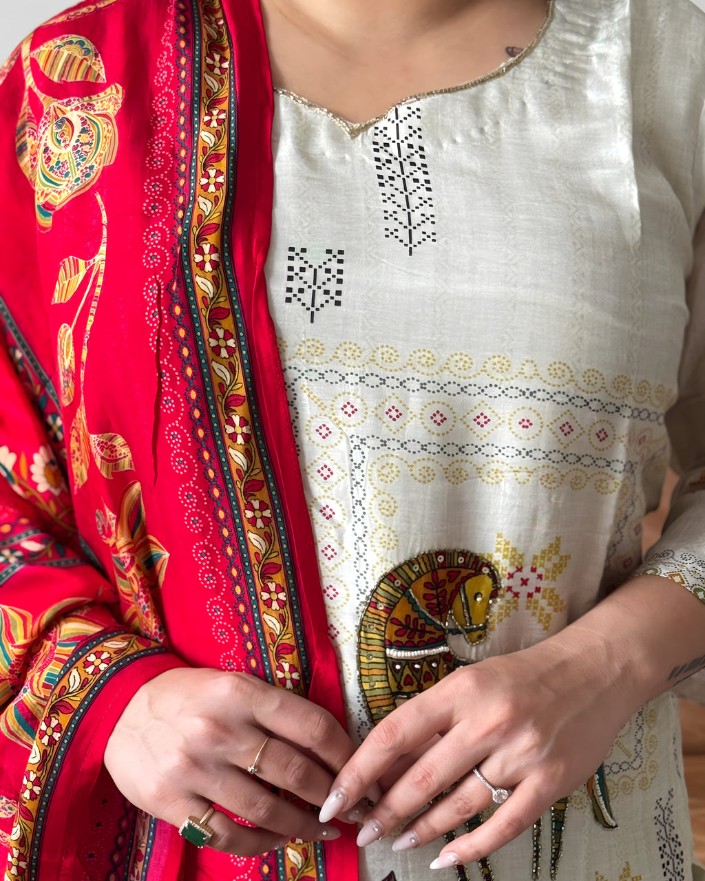 Person wearing a red and gold embroidered traditional outfit with a white blouse featuring intricate patterns.