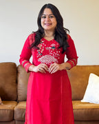 Woman wearing a red traditional outfit with white embroidery in a living room.