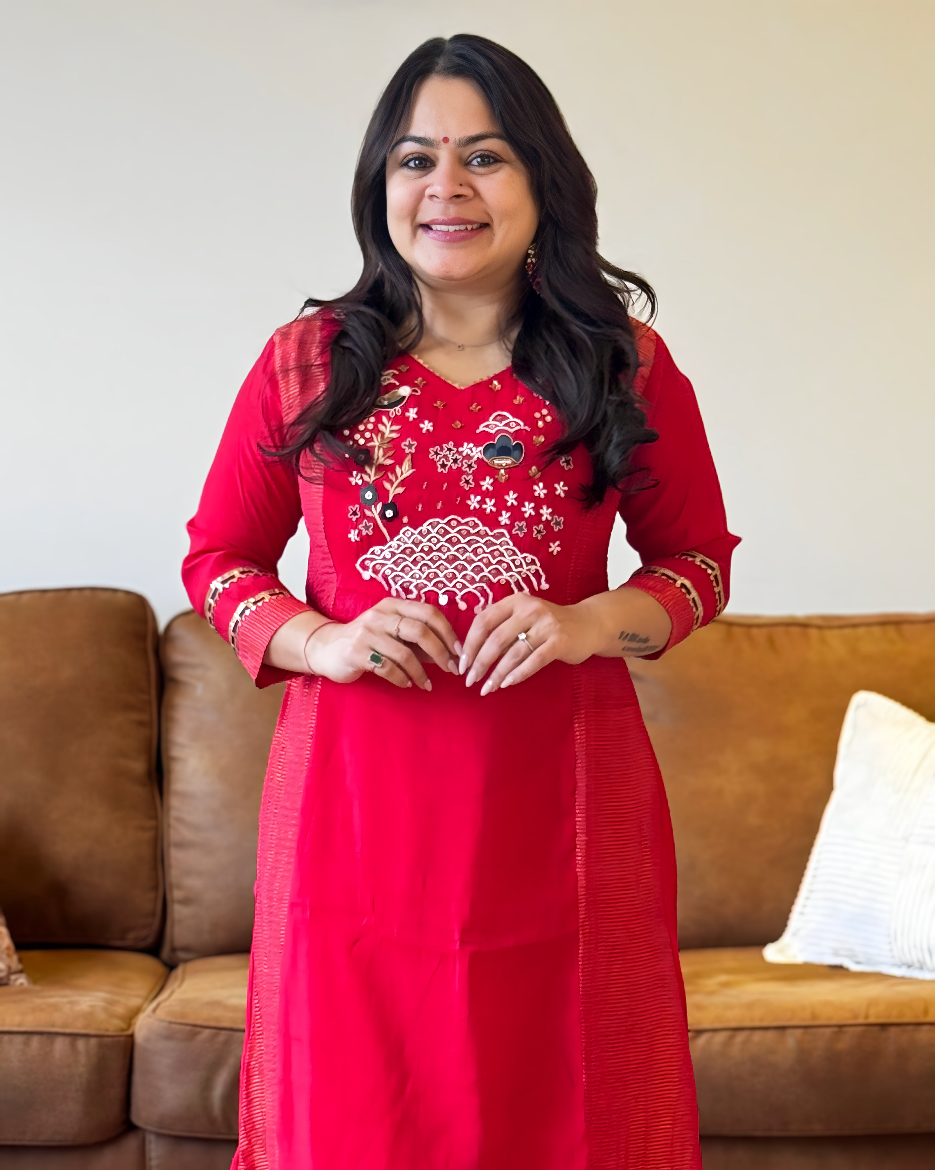 Woman wearing a red traditional outfit with white embroidery in a living room.
