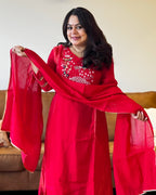 Woman wearing a red traditional outfit with a matching dupatta, holding it in front of her.
