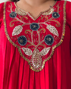 Close-up of a red embroidered garment with a V-neckline, featuring ornate floral and vine embroidery in gold, silver, and navy blue, accented with coin trim.