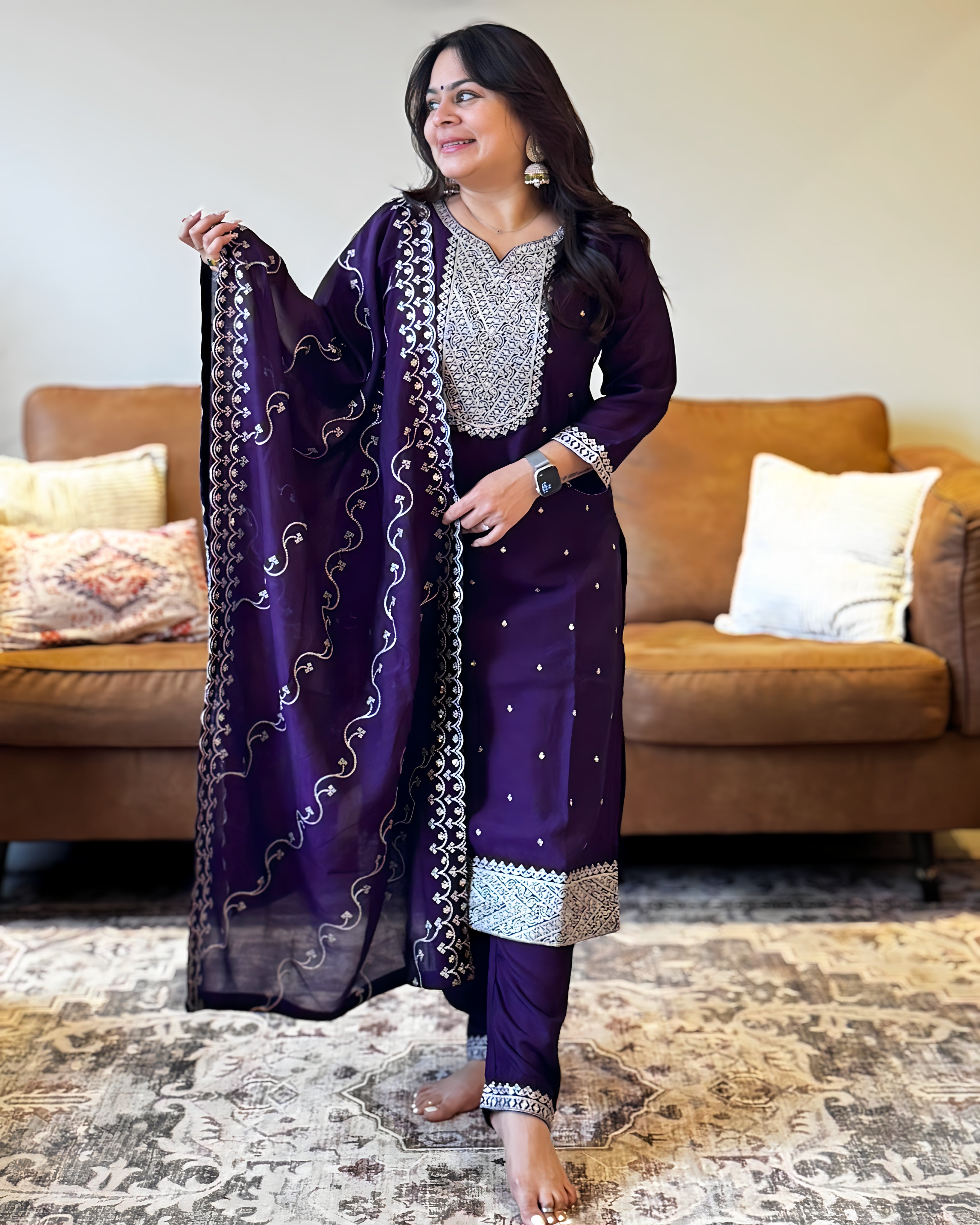 Woman in a purple traditional outfit with silver details in a living room setting.