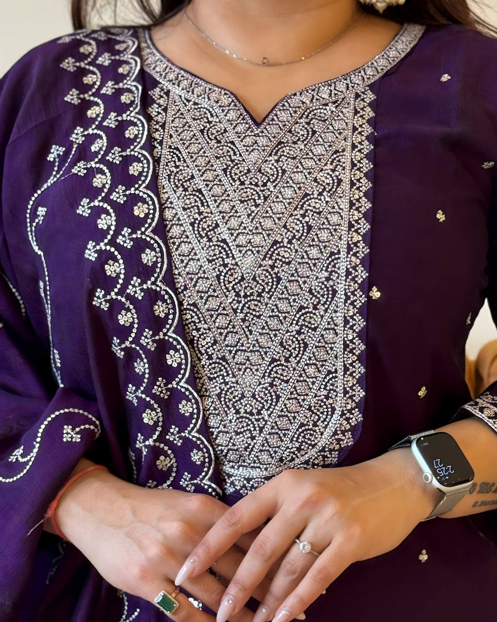 Close-up of a person wearing a purple outfit with intricate white embroidery, showing a watch and ring.