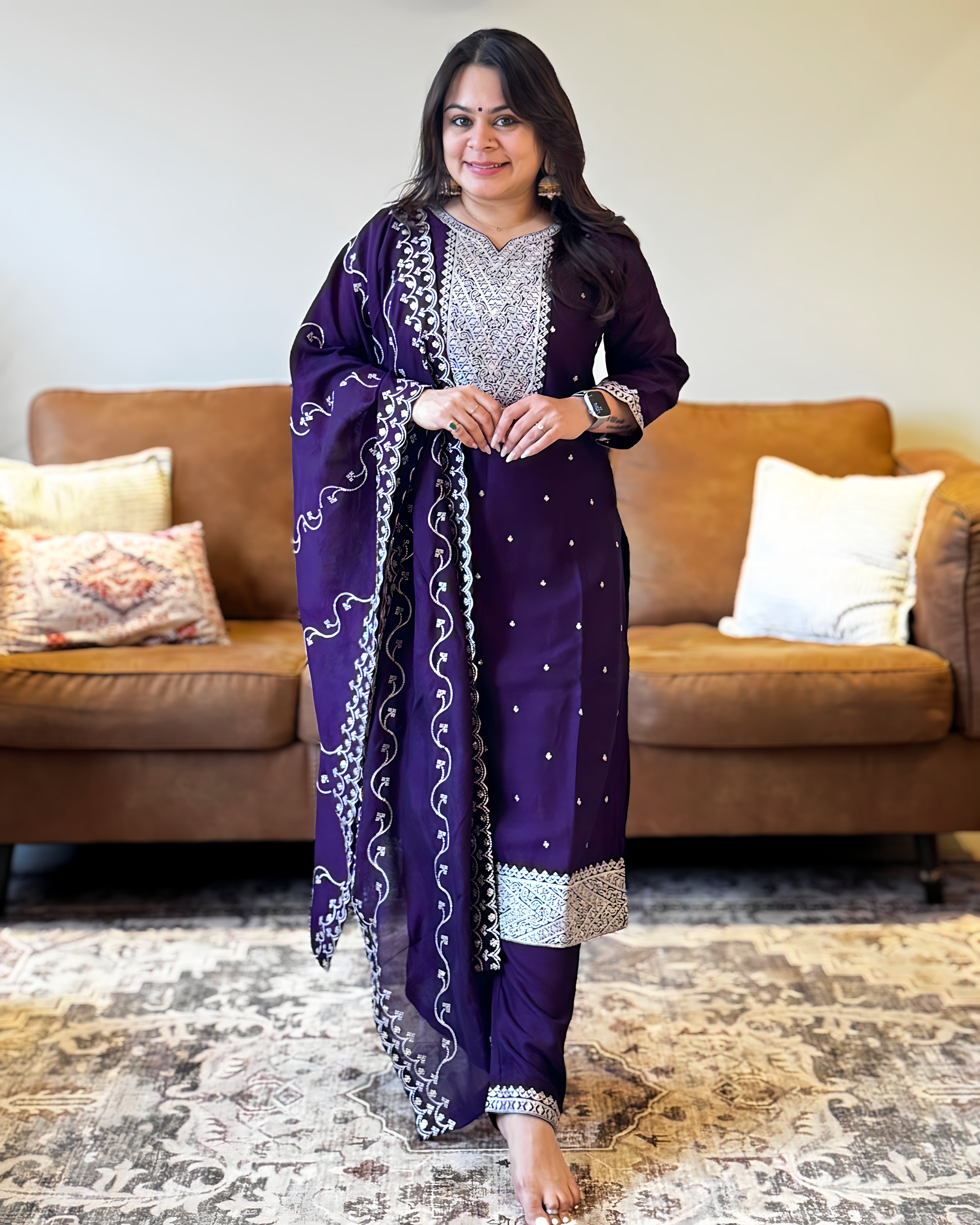 Woman wearing a purple traditional outfit with a matching dupatta in a living room.