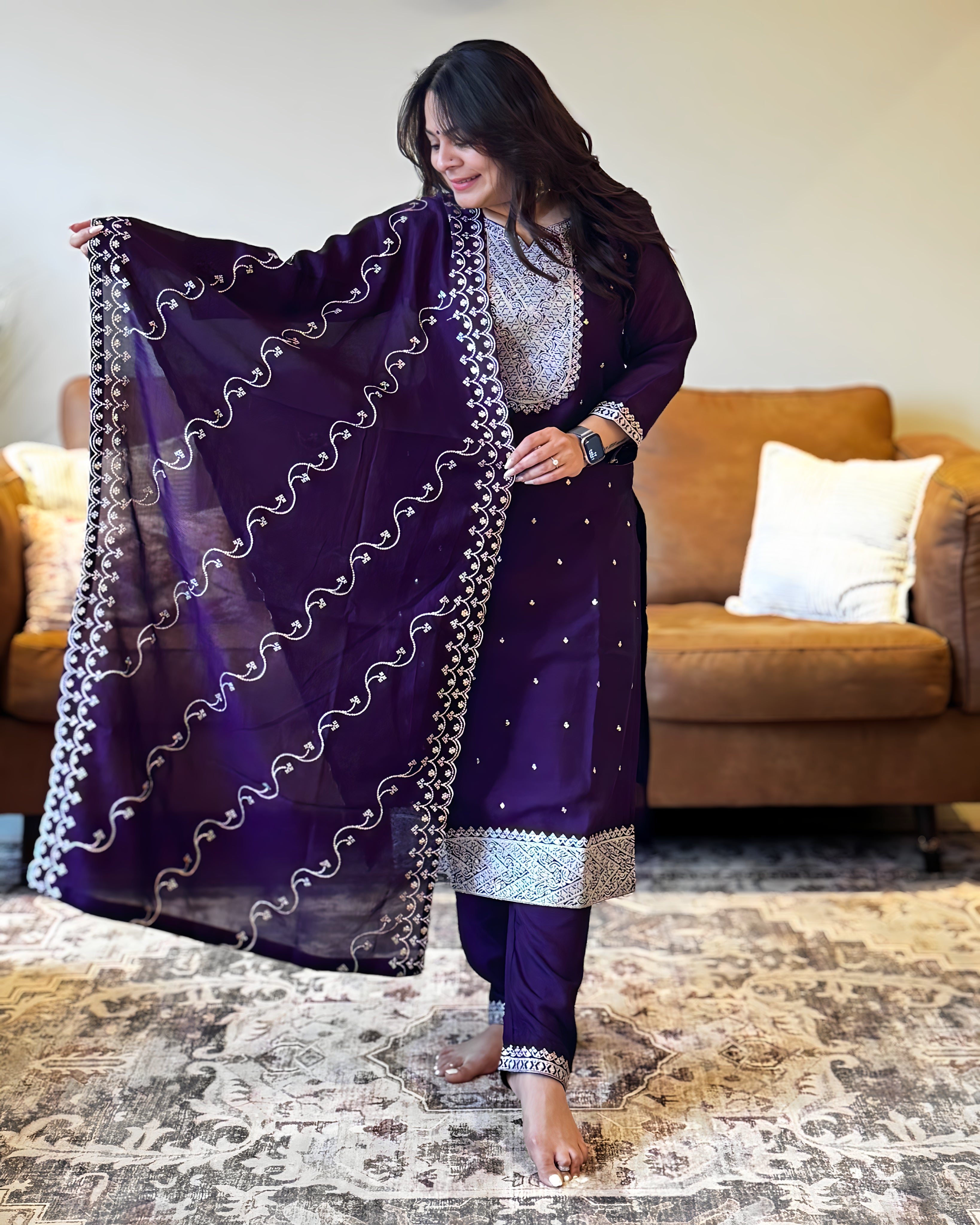 Woman in a purple traditional outfit with a matching dupatta in a living room.