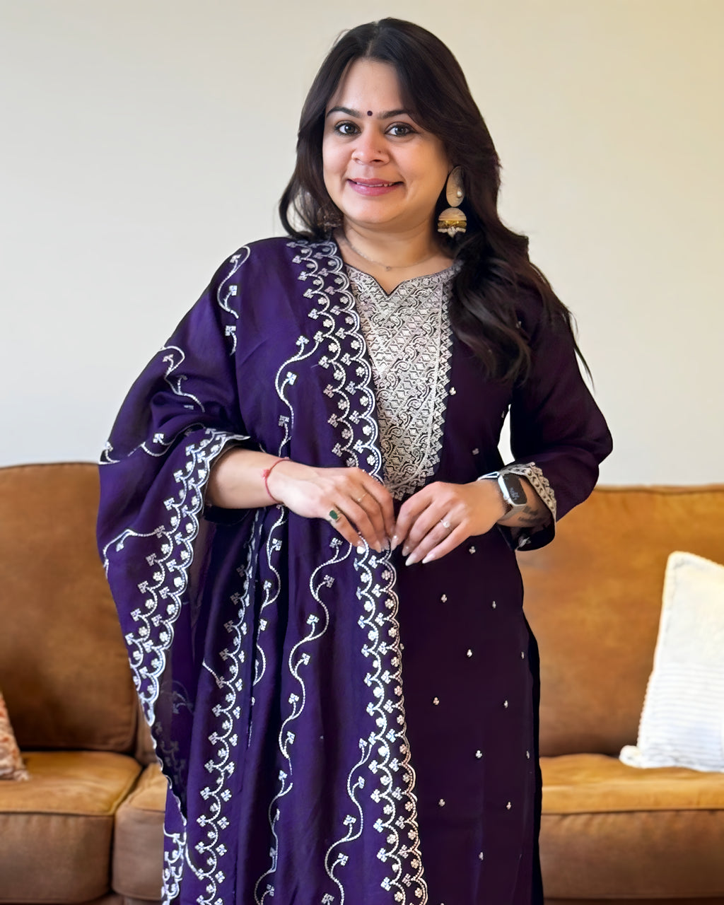 Woman wearing a purple traditional outfit with white patterns in a living room setting.