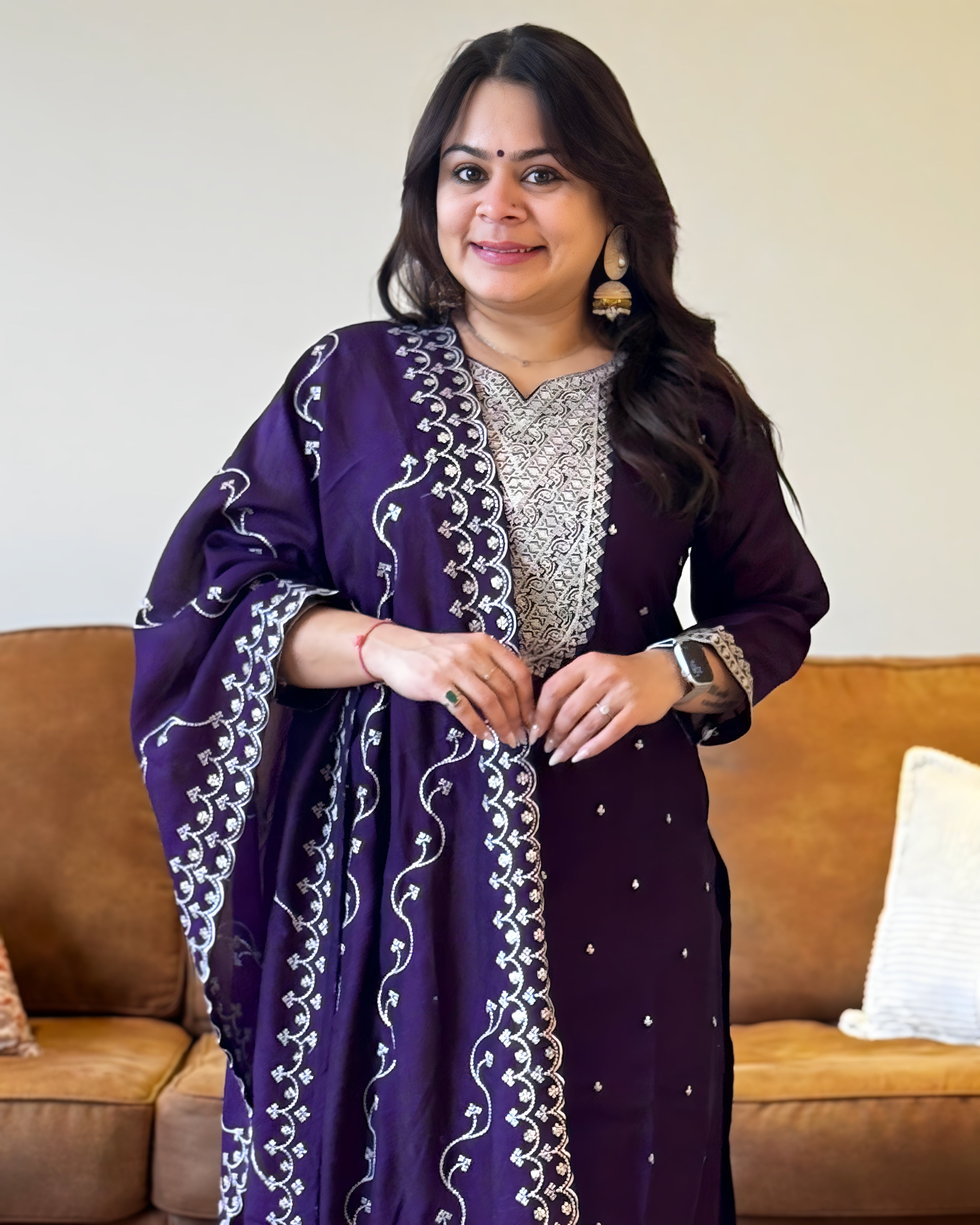 Woman wearing a purple traditional outfit with white patterns in a living room setting.