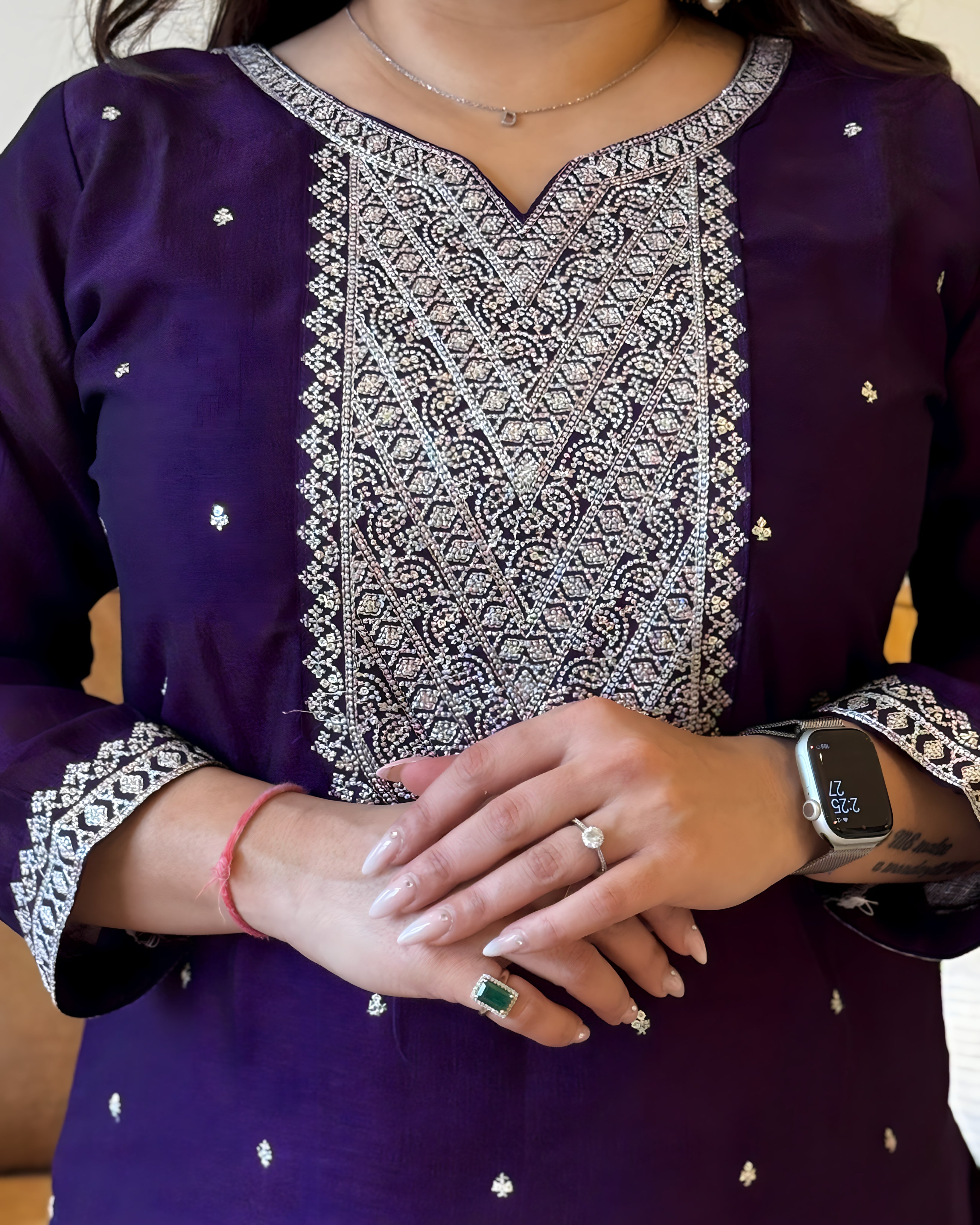 Person wearing a purple embroidered outfit with jewelry and a smartwatch.