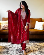 Woman in a red traditional outfit with white patterns standing in a living room.