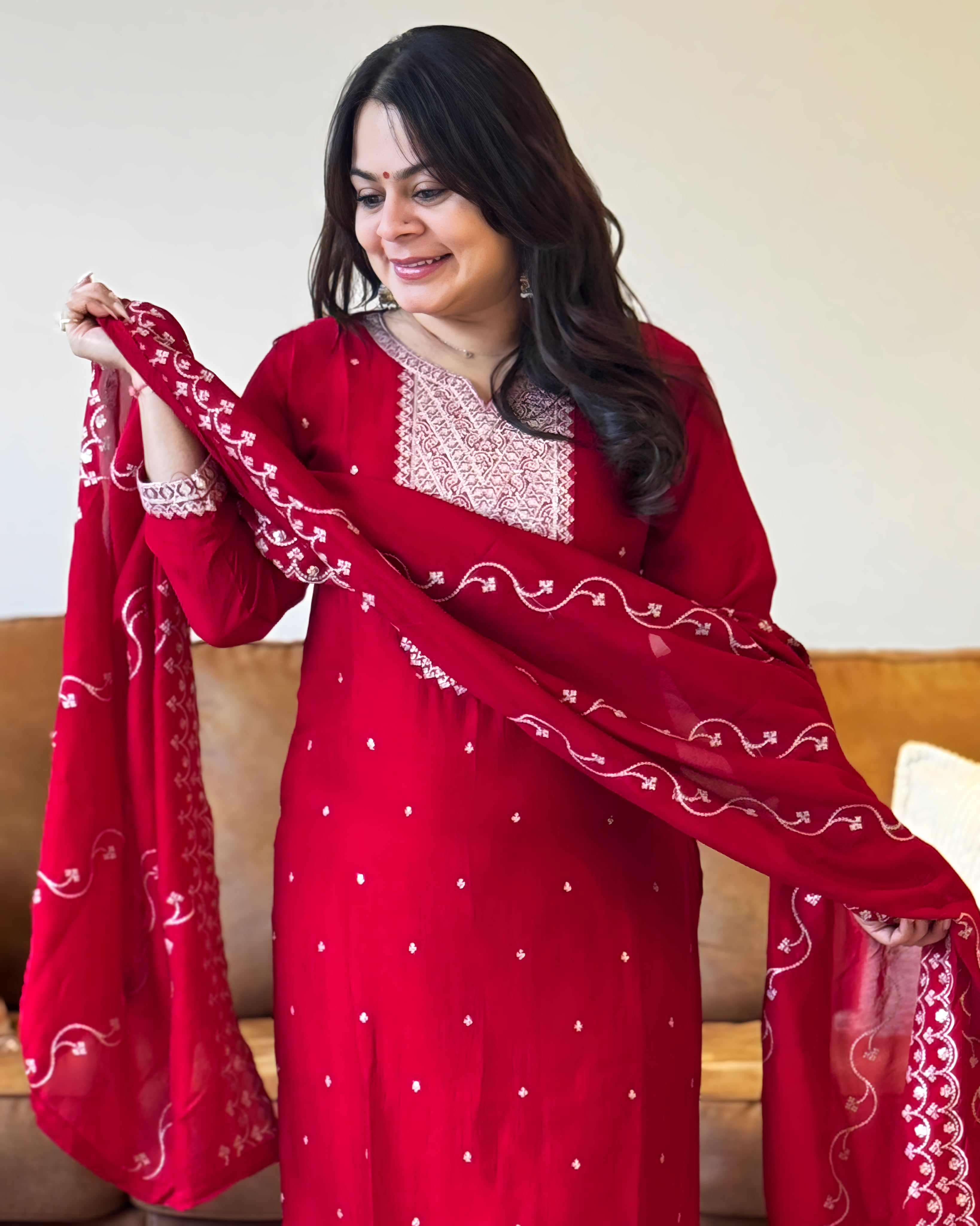 Woman wearing a red traditional outfit with white patterns, holding a matching dupatta.
