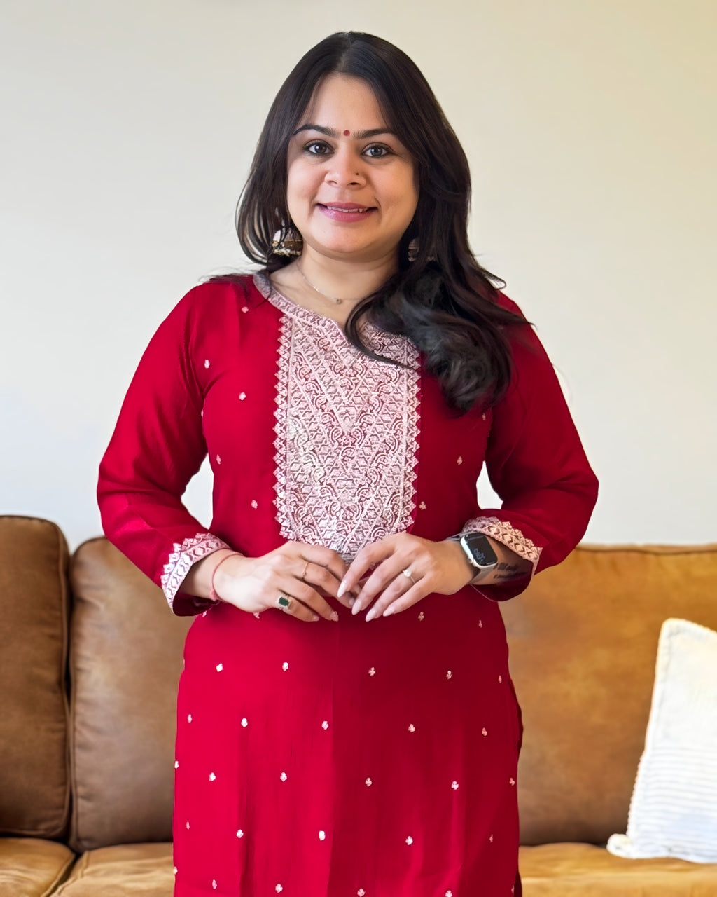 Woman wearing a red traditional outfit with white patterns in a living room setting.