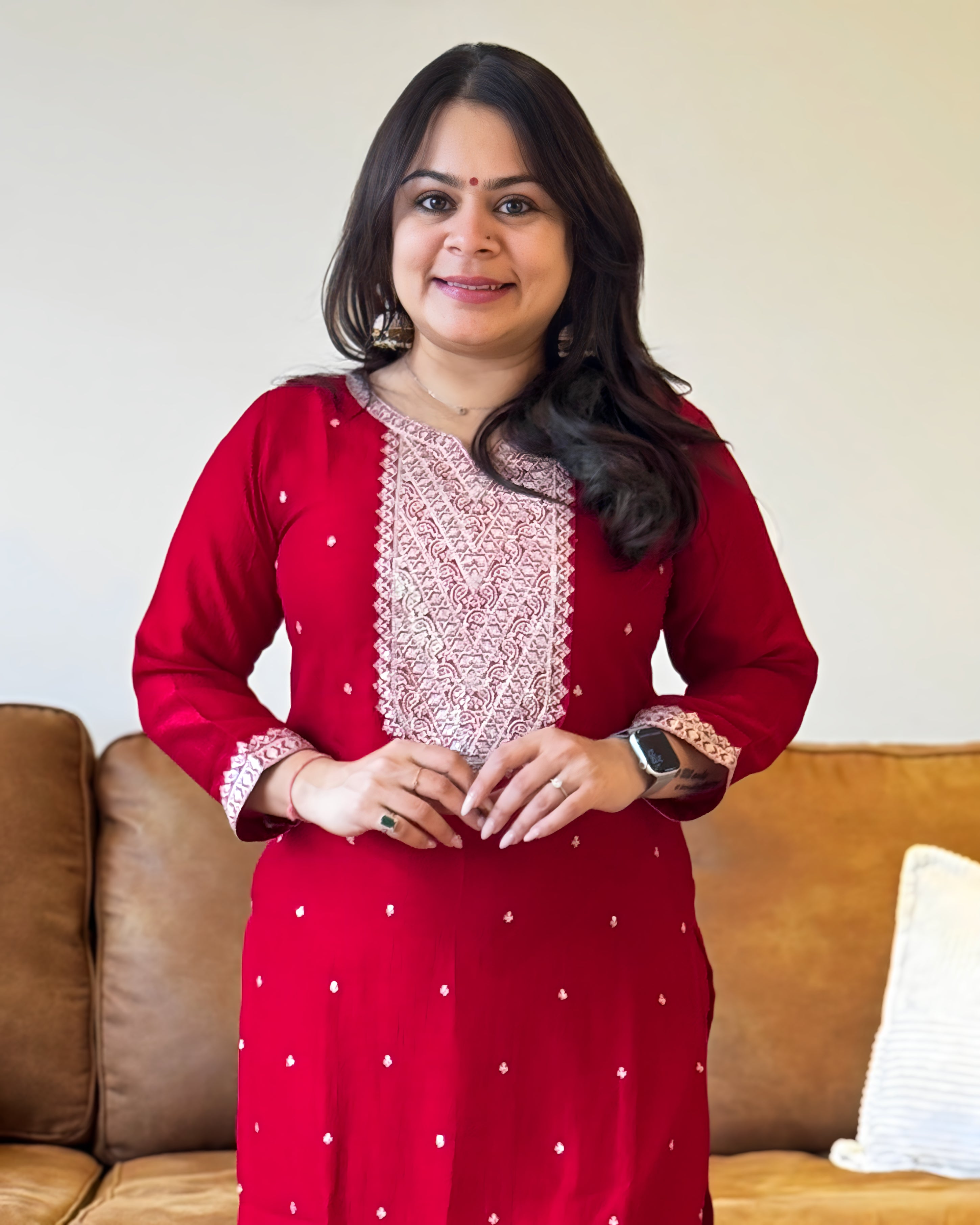 Woman wearing a red traditional outfit with white patterns in a living room setting.