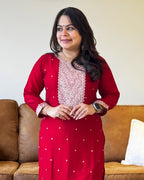Woman wearing a red traditional outfit with white patterns in a living room setting.
