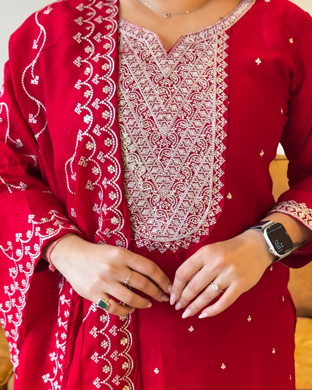 Red embroidered traditional outfit with white patterns, close-up of hands.