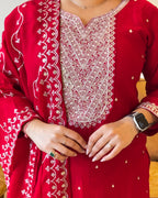 Red embroidered traditional outfit with white patterns, close-up of hands.