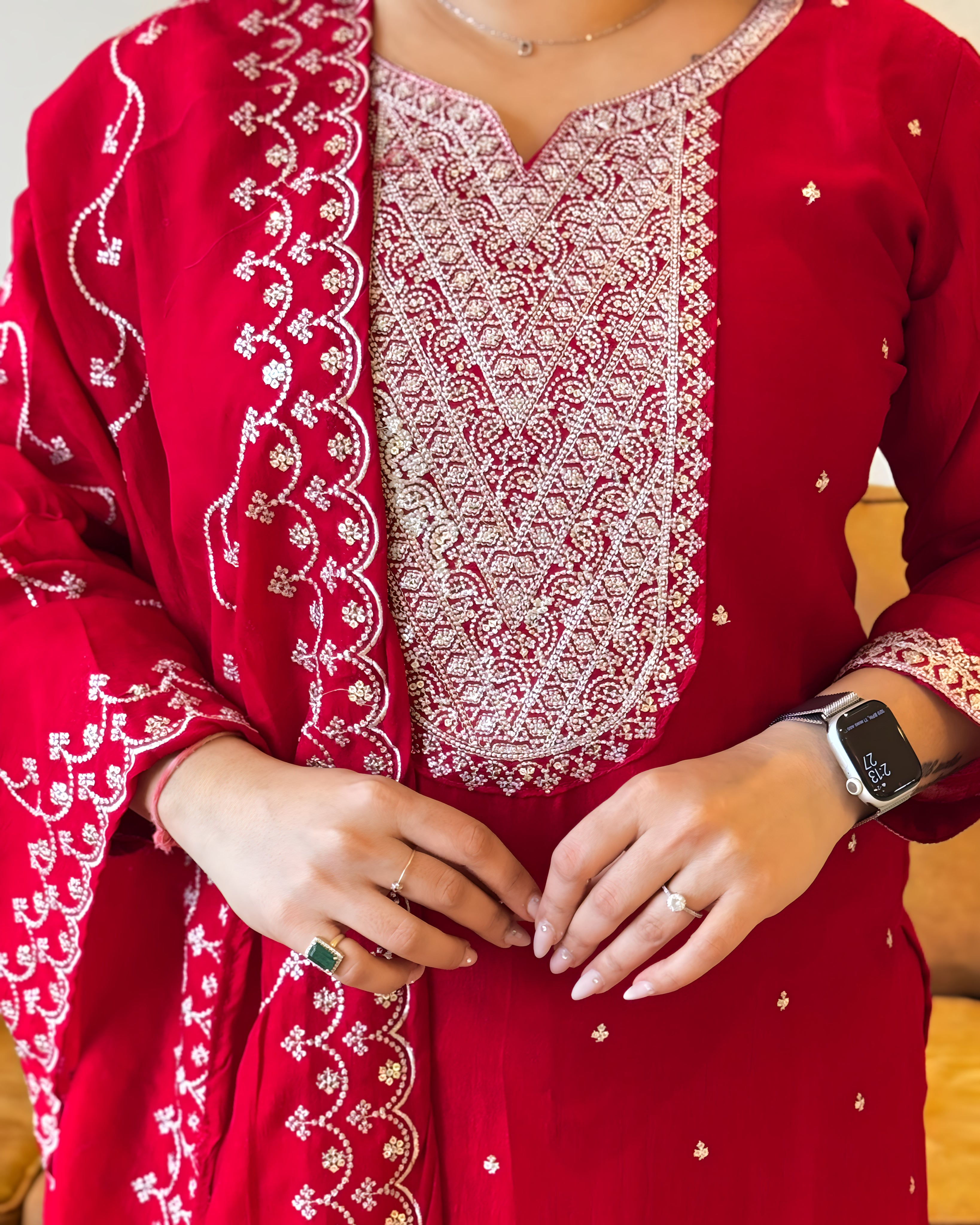 Red embroidered traditional outfit with white patterns, close-up of hands.