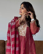 A woman wearing a traditional Indian outfit in dusty rose and gold, with a matching striped dupatta, posing indoors.