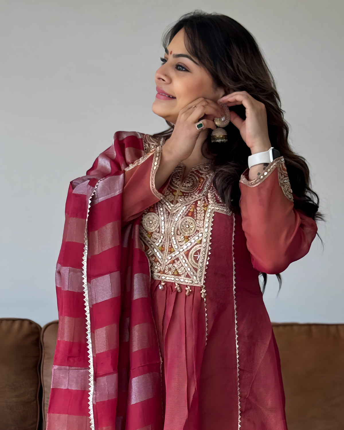 A woman wearing a traditional Indian outfit in dusty rose and gold, with a matching striped dupatta, posing indoors.