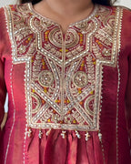Close-up of a traditional embroidered red and gold kurta or anarkali, showing intricate mirror work and beadwork on the chest panel.