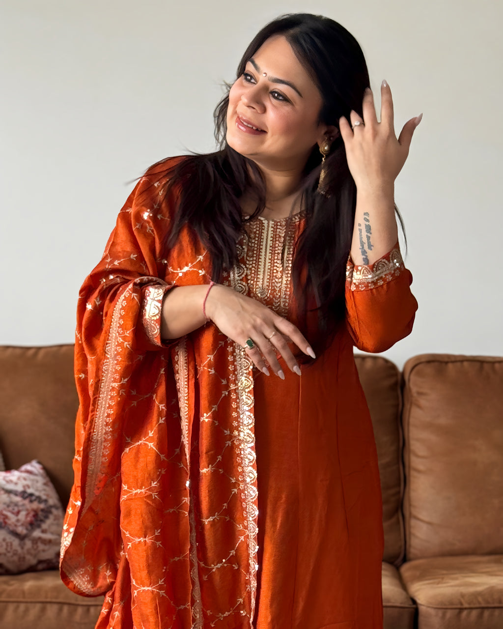Woman in an orange traditional outfit standing in a room with a couch.