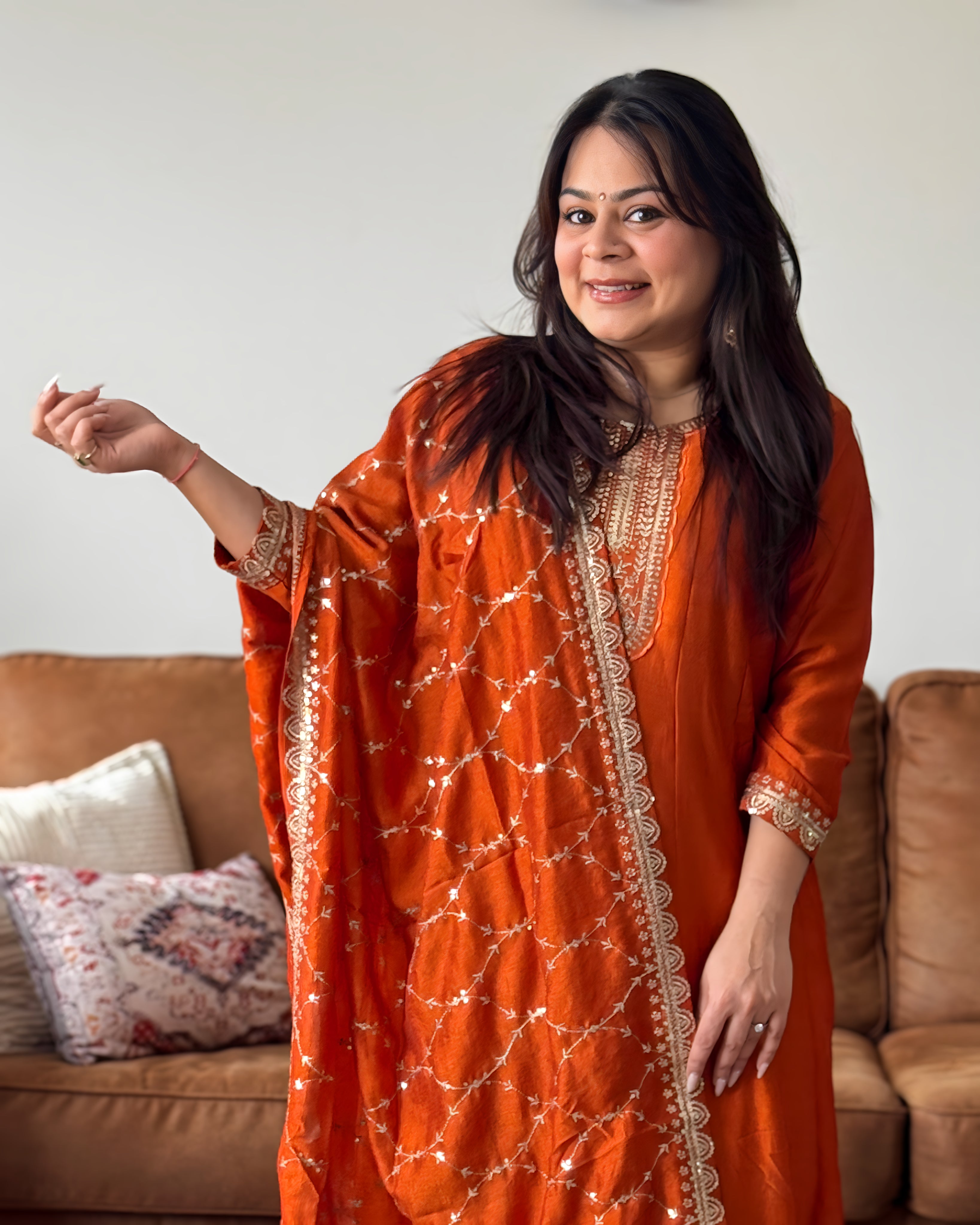 Woman in an orange traditional outfit standing in a living room.