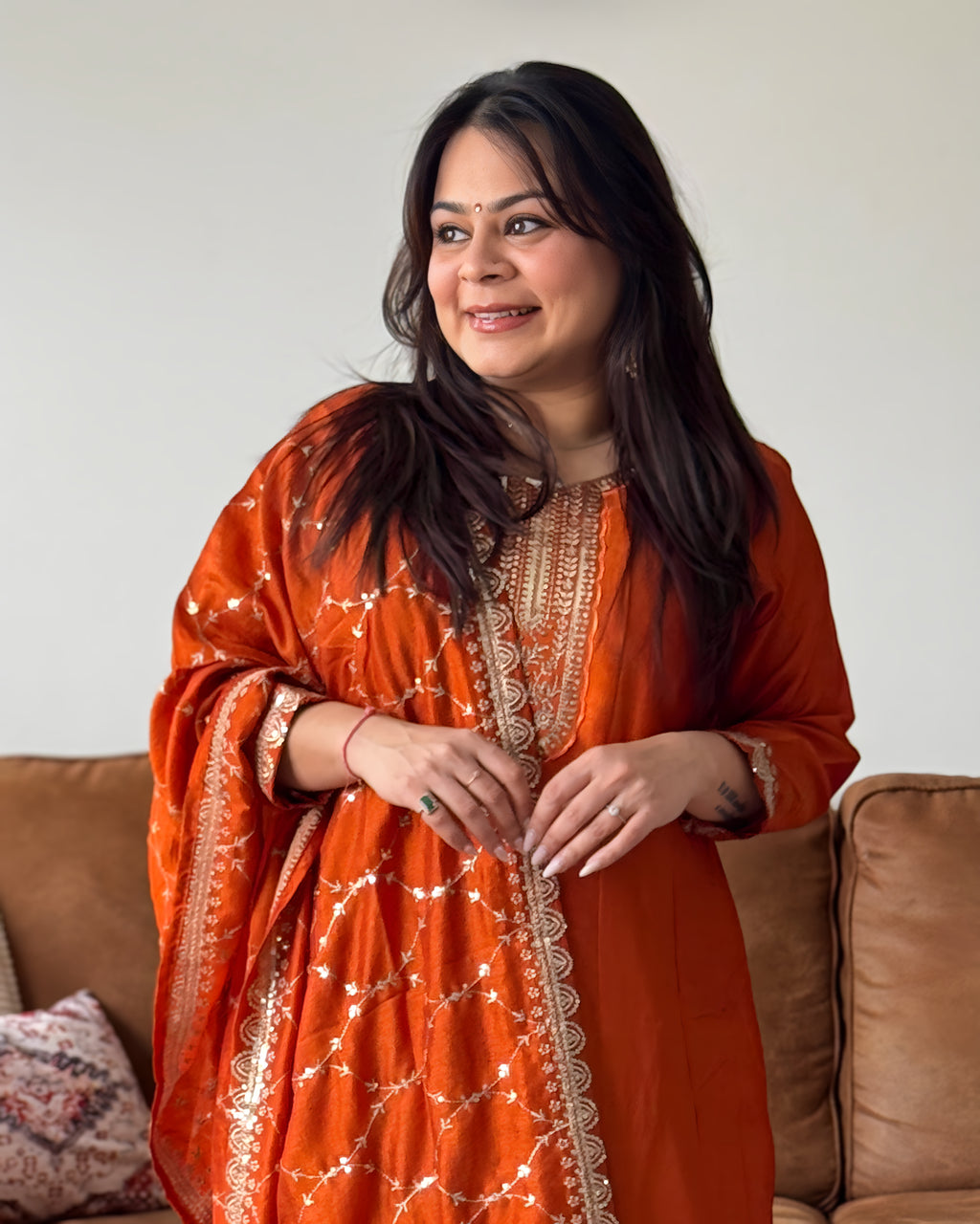 Woman wearing an orange traditional outfit sitting on a couch.