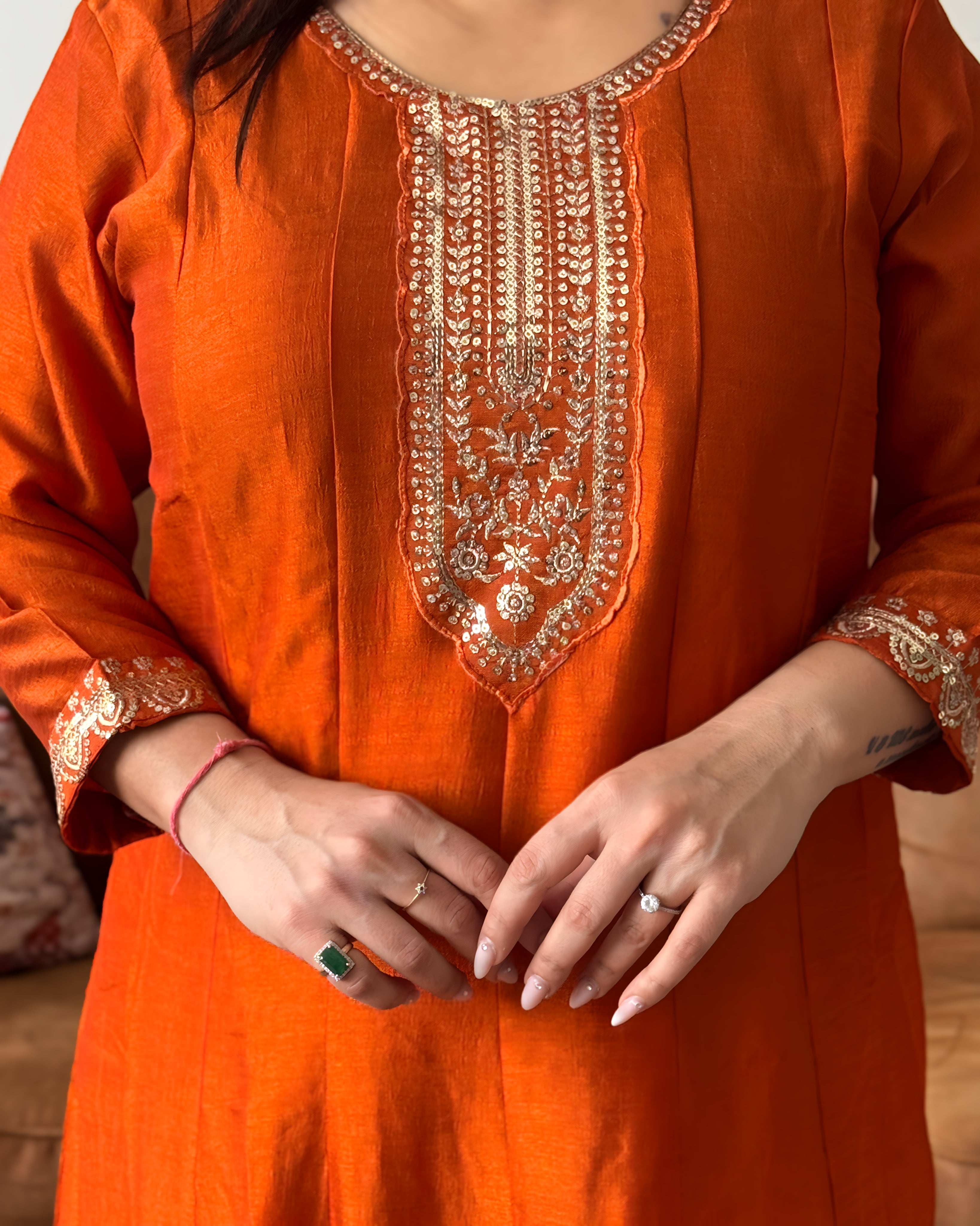 Orange traditional outfit with intricate gold embroidery on a neutral background