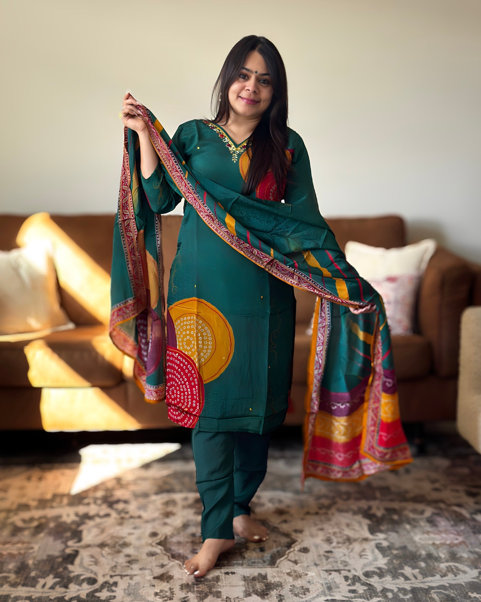 Woman in traditional green outfit with a colorful scarf in a living room setting