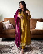 Woman in a yellow traditional outfit with a purple dupatta standing in a living room.