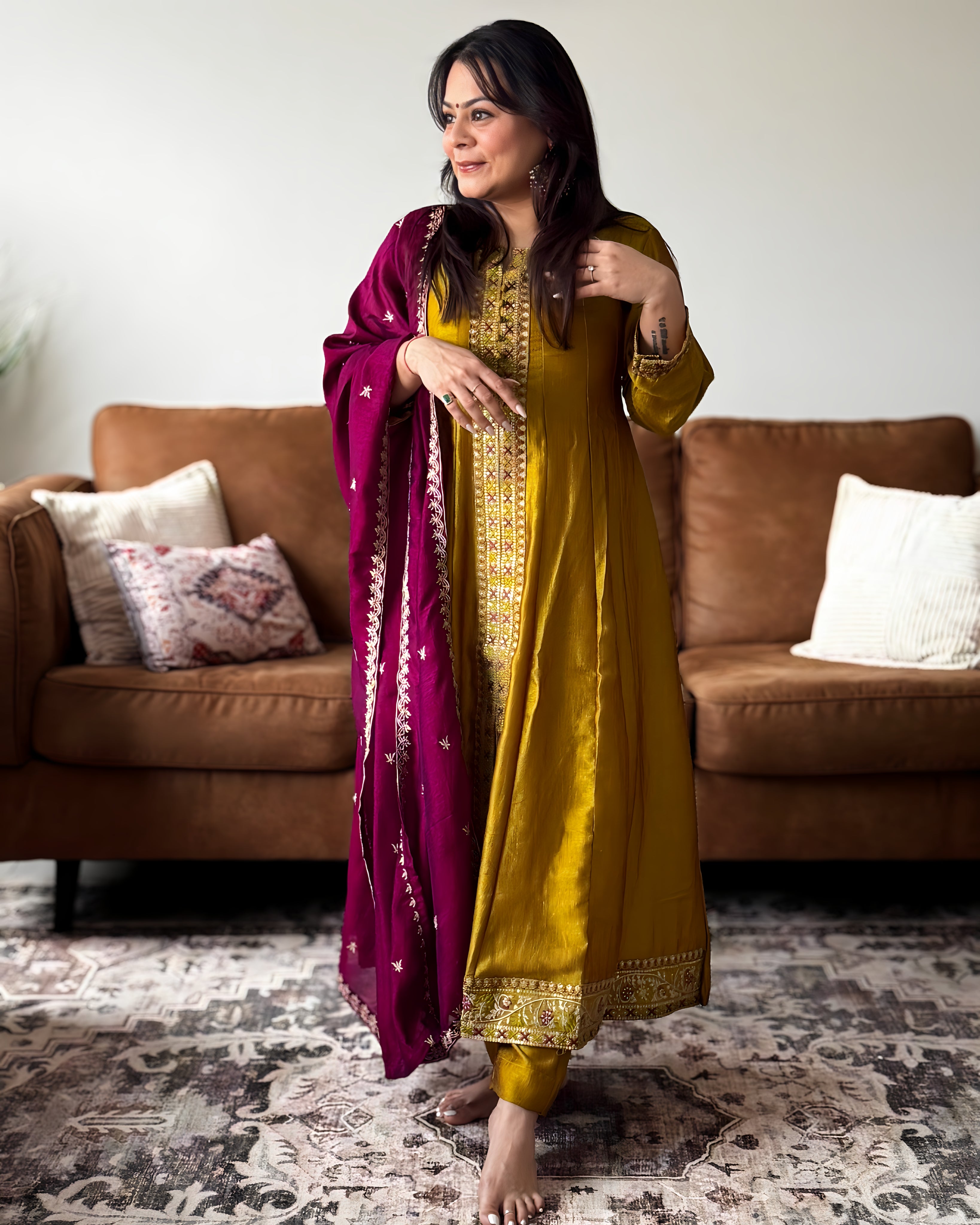 Woman in a yellow traditional outfit with a purple dupatta standing in a living room.