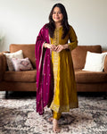 Woman in a yellow traditional outfit with a pink dupatta standing in a living room.