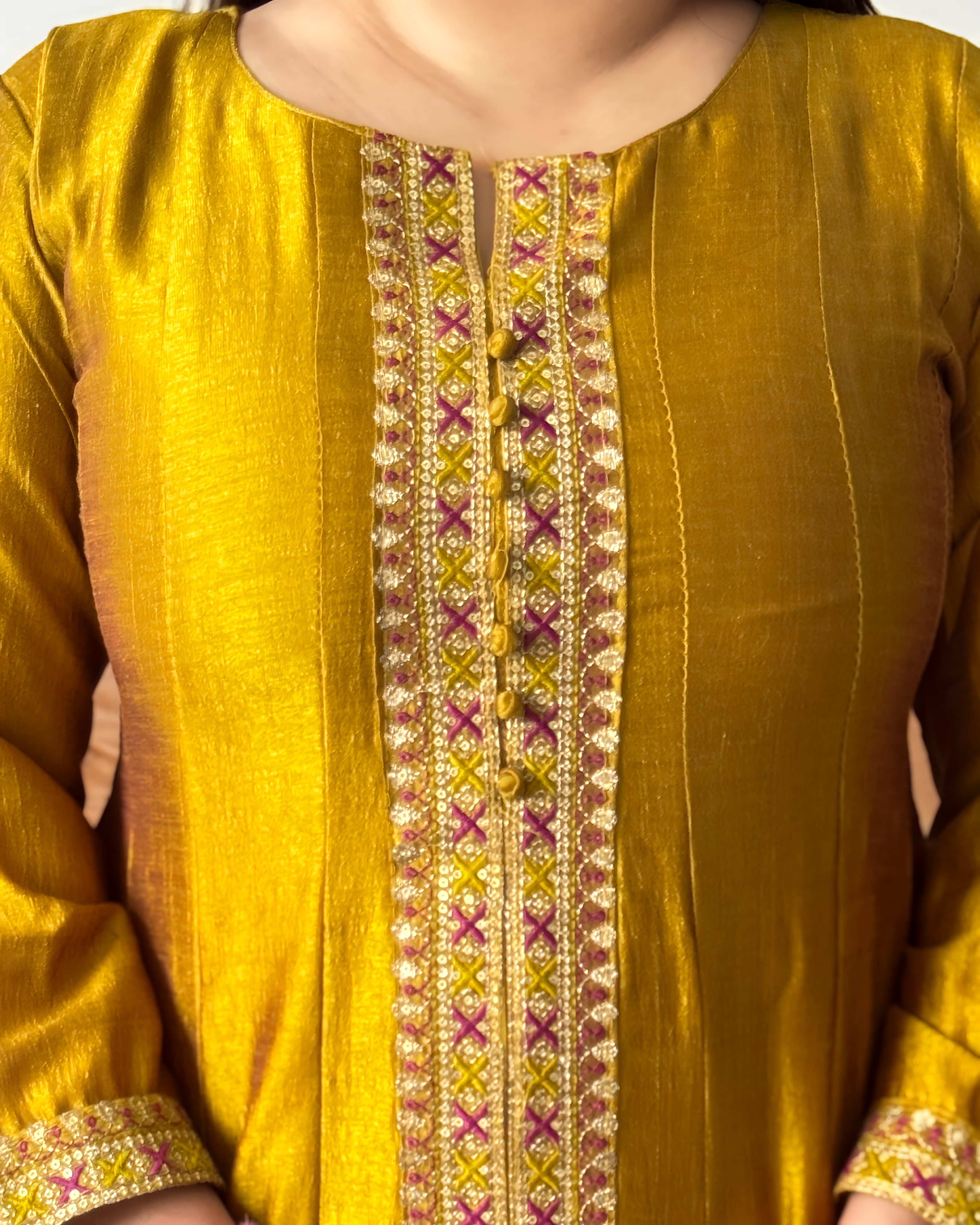 Woman in a green traditional outfit standing in a living room with a brown sofa and patterned rug.